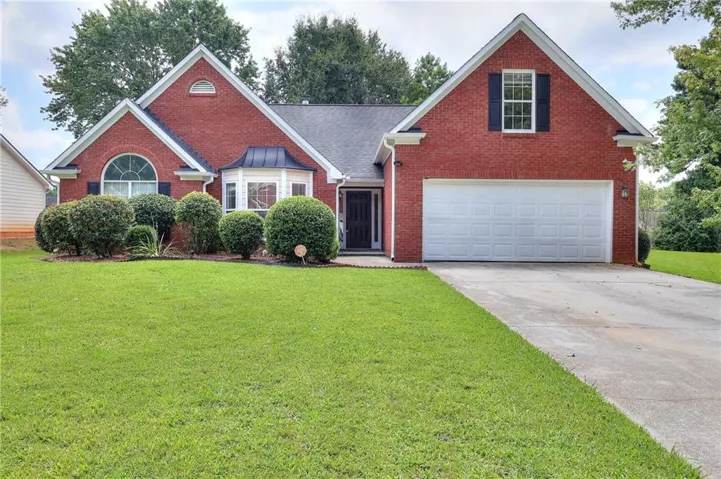 Red brick facade with white trim, arched window, bay window, two-car garage, and mature landscaping
