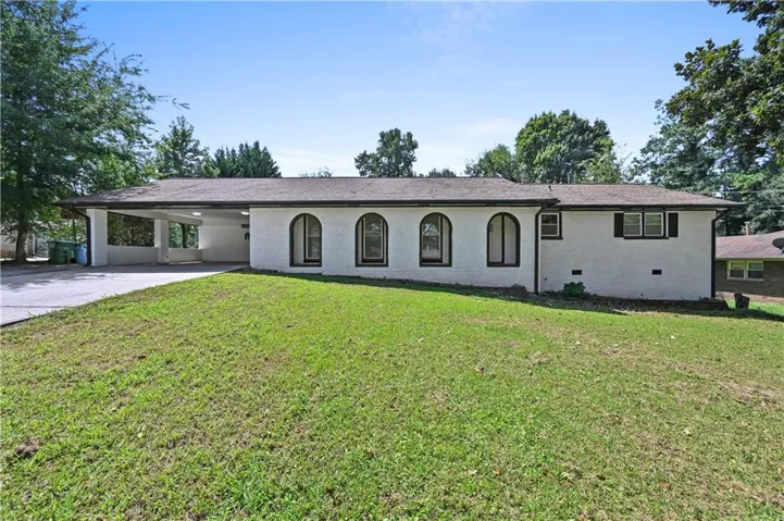 White exterior with arched windows, a covered carport, and a dark shingle roof