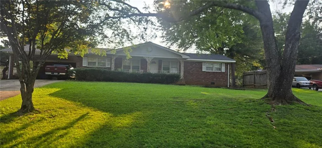 WITH NEW ROOF AND NEW AC JUST INSTALLED Brick ranch-style residence featuring a prominent front lawn, established trees, an attached carport, and a covered front entry with decorative columns