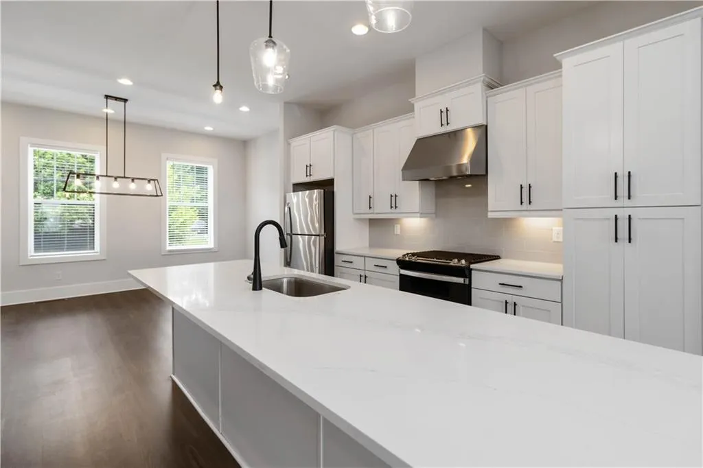 Kitchen with stainless steel appliances, under cabinet range hood, dark wood-style floors, white cabinets, and decorative backsplash
