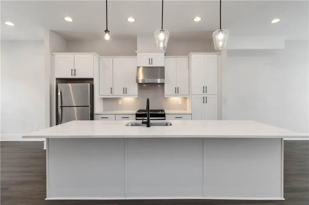 Kitchen featuring freestanding refrigerator, under cabinet range hood, white cabinets, a kitchen island with sink, and recessed lighting