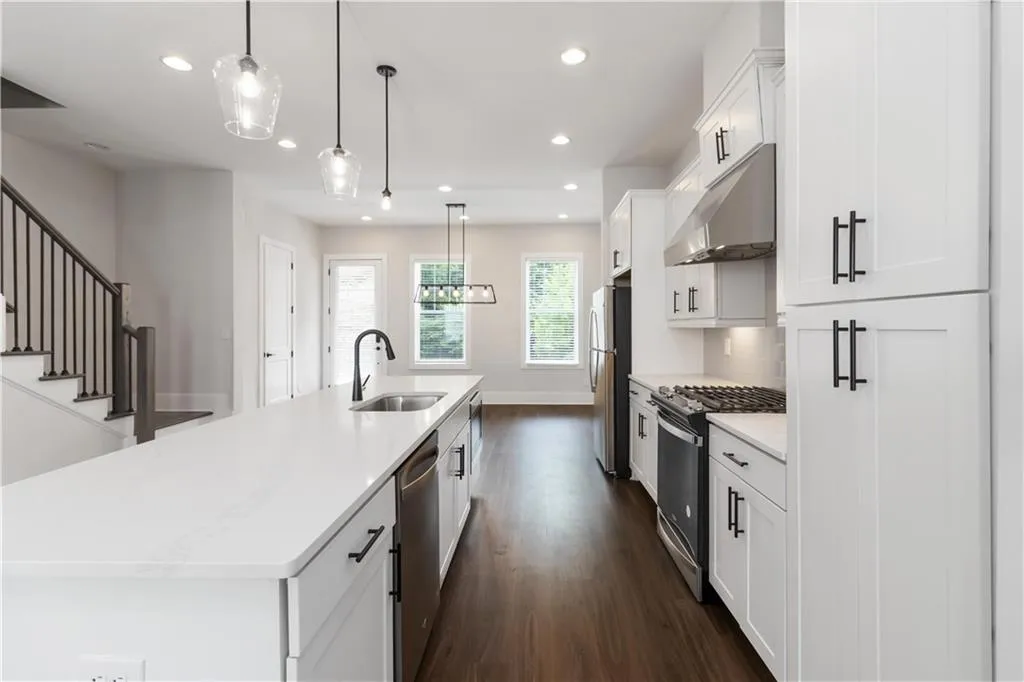 Kitchen with stainless steel appliances, under cabinet range hood, a kitchen island with sink, white cabinets, and recessed lighting