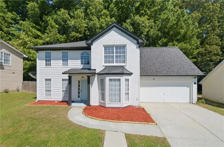 White exterior with dark trim accents, bay window, two-car garage, and a covered entry