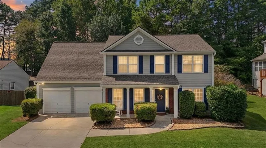 Two-story residence featuring a covered front porch, a two-car garage, and mature landscaping