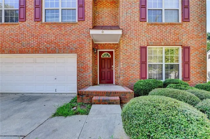 Brick exterior with an arched entryway, white garage door, and red window shutters