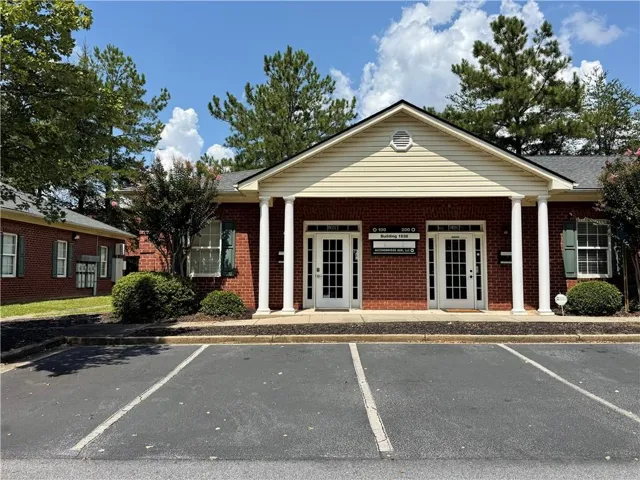 Brick exterior with gabled roofline and multiple entryways, featuring white columns and dark green shutters