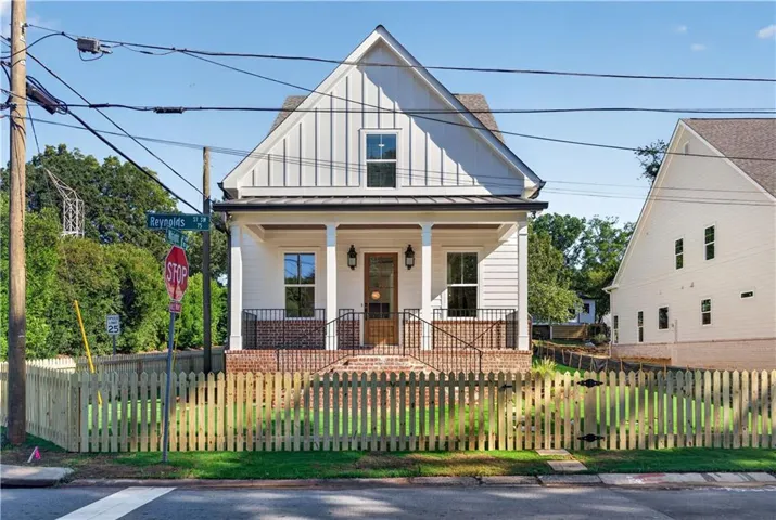 Classic gabled facade with board and batten siding, a covered front porch, brick foundation, and a picket fence