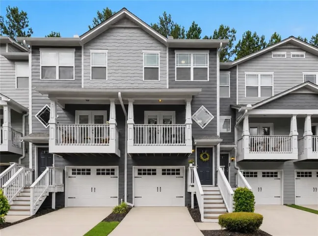 Contemporary townhome community featuring elegant gray fiber cement siding, dual two-car garages with paneled doors, tiered front porches with white railings, and manicured landscaping with mature trees