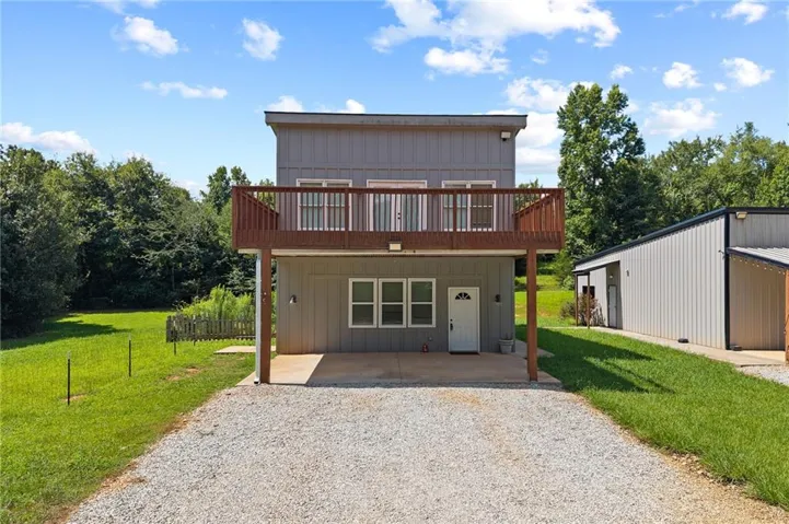 Multi-story residence featuring a second-level balcony, ground-level covered patio, and a gravel driveway