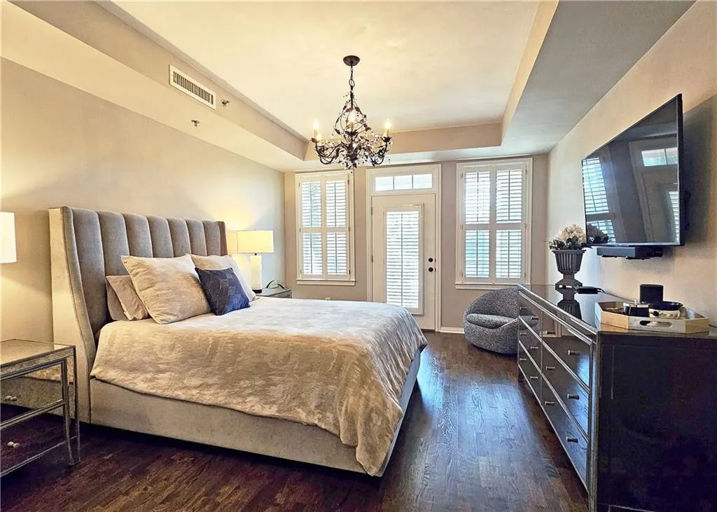 Bedroom with a raised ceiling, a chandelier, dark wood-style flooring, and multiple windows