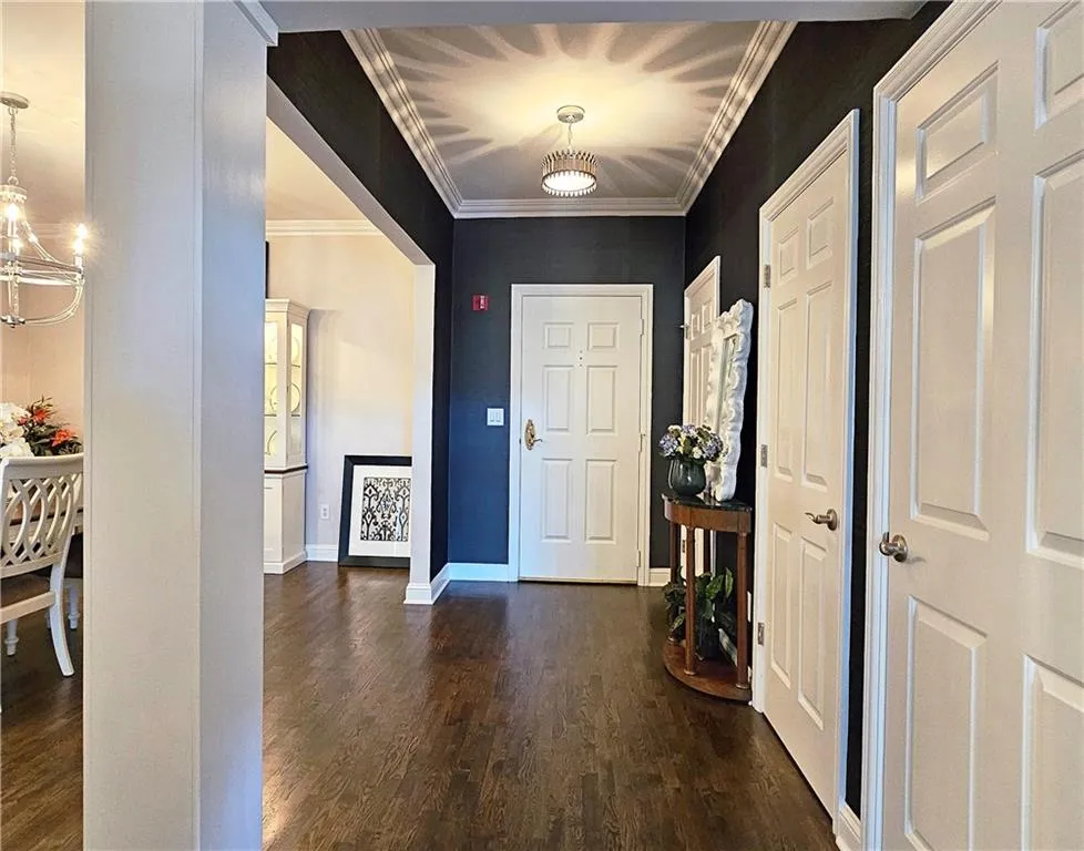 Entrance foyer with dark wood-type flooring, crown molding, and a chandelier