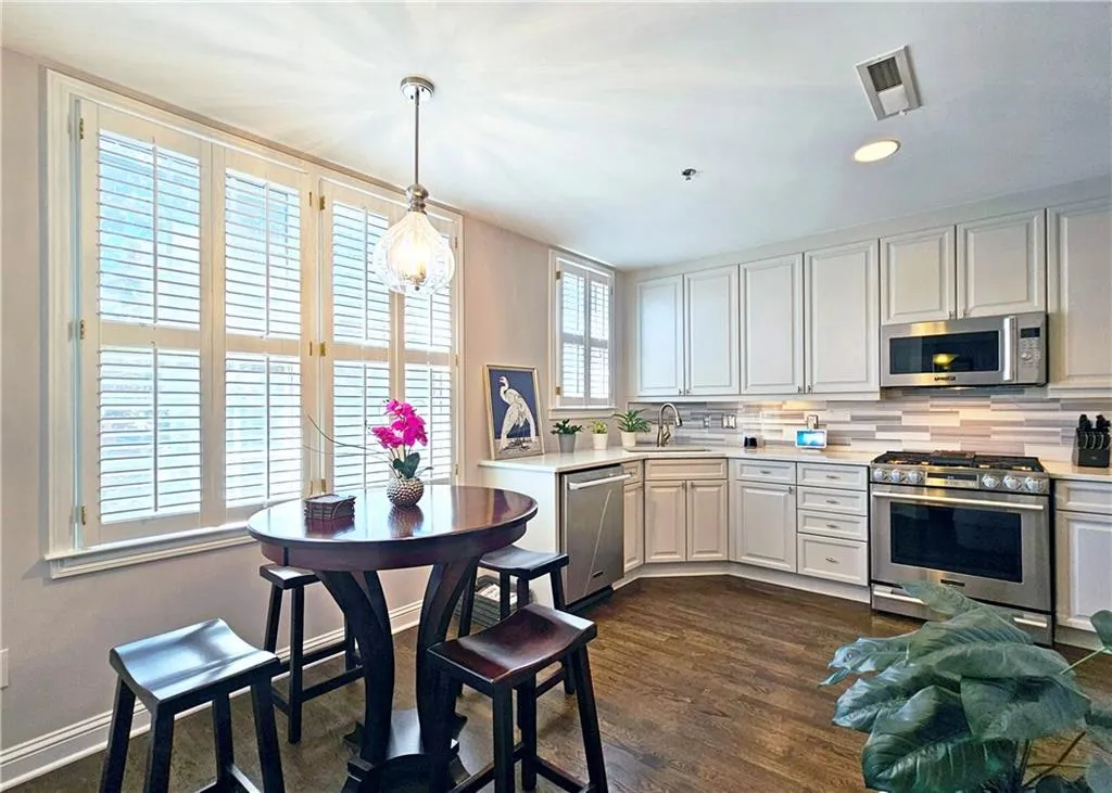 Kitchen featuring stainless steel appliances, light countertops, backsplash, pendant lighting, and dark wood-type flooring