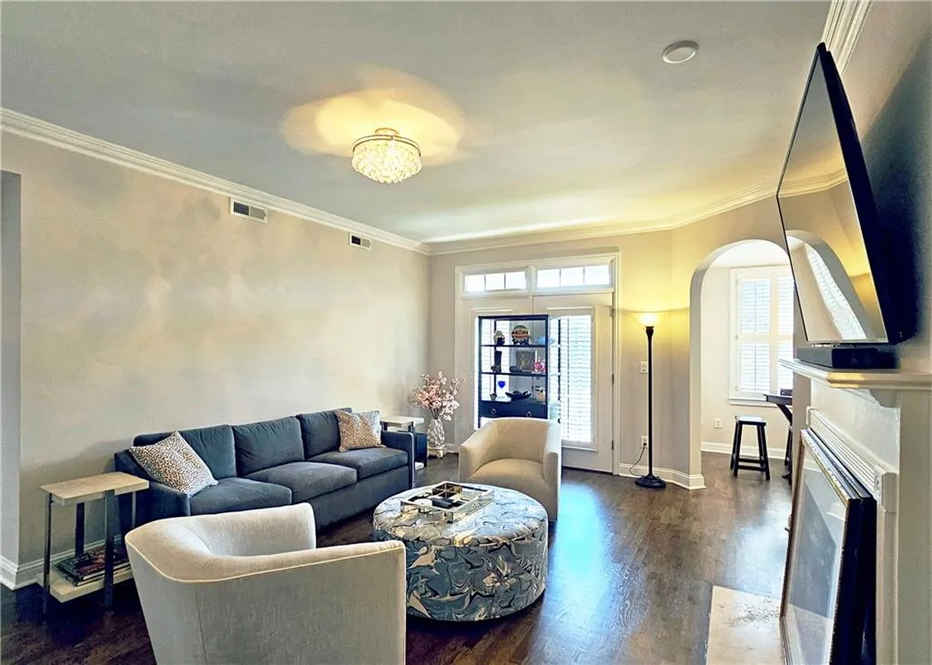 Living area with arched walkways, dark wood-type flooring, ornamental molding, and a fireplace with flush hearth