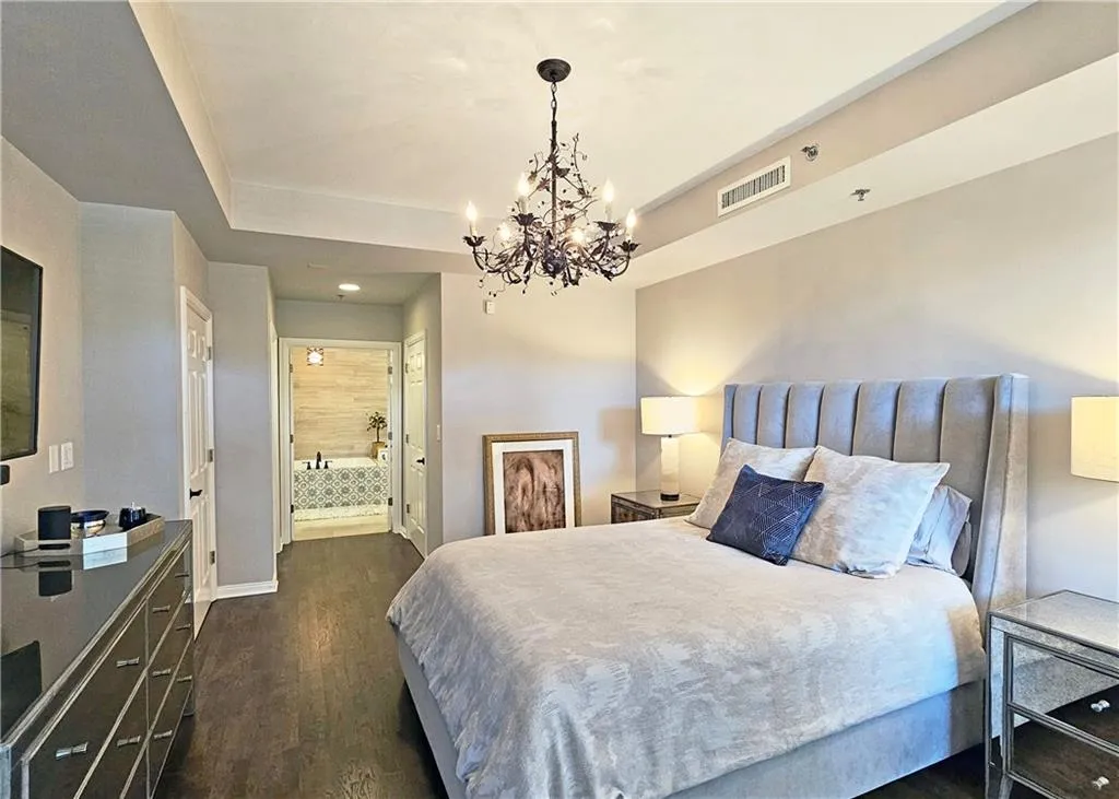 Bedroom with dark wood-style floors, a chandelier, a raised ceiling, ensuite bathroom, and recessed lighting