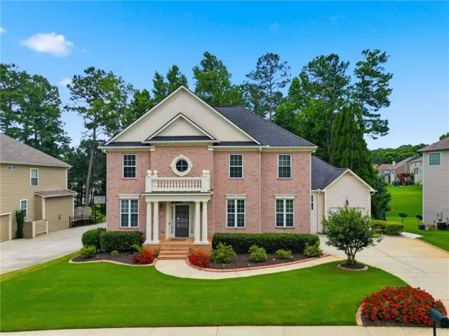 Brick facade residence featuring a covered front entry with columns, a second-story balcony with balustrade, and an arched window