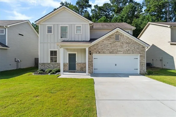 Two-story residence featuring light-colored siding and brick accents, a covered entry, an attached two-car garage, and a concrete driveway