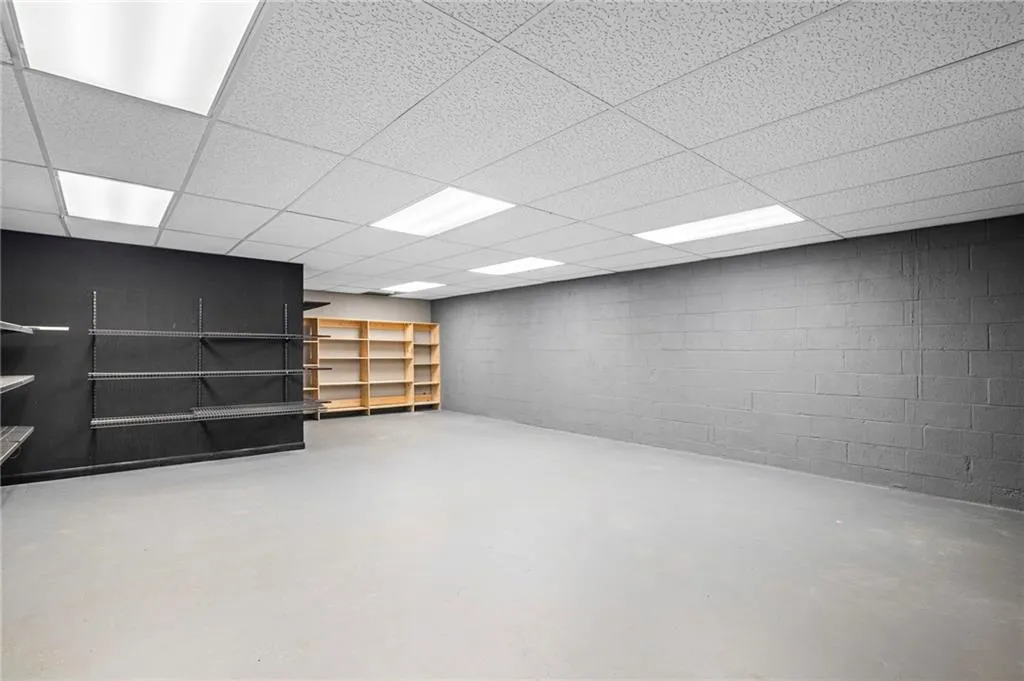 Finished basement featuring concrete walls and flooring and drop lighting with integrated shelves