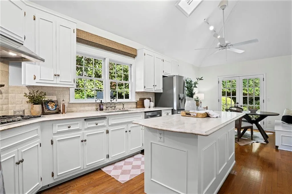 Kitchen featuring light stone counters, a center island, white cabinetry, dark wood finished floors, and vaulted ceiling