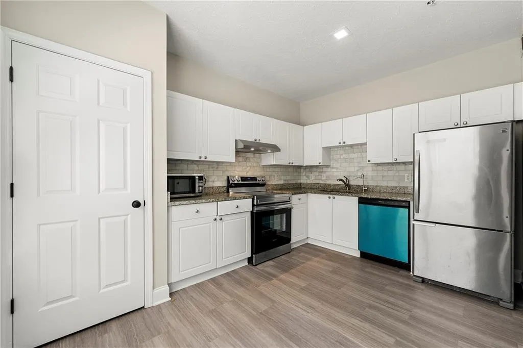 Kitchen with stainless steel appliances, white cabinets, light hardwood / wood-style floors, and tasteful backsplash