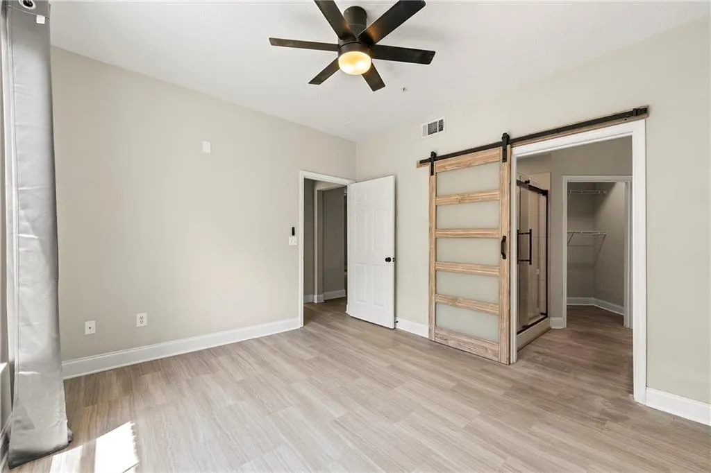 Unfurnished bedroom featuring light hardwood / wood-style flooring, a spacious closet, a barn door, a closet, and ceiling fan