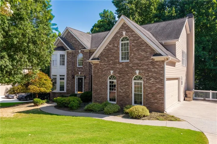 Brick Colonial home featuring a two-story facade with arched window details, multiple gabled rooflines, and a circular driveway