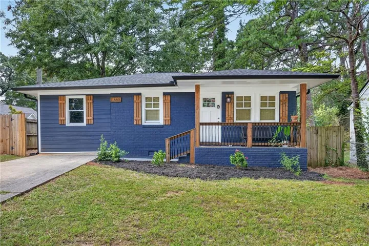 Inviting front porch with wood columns and black railing, blue exterior with wood shutters, concrete driveway, and mature landscaping
