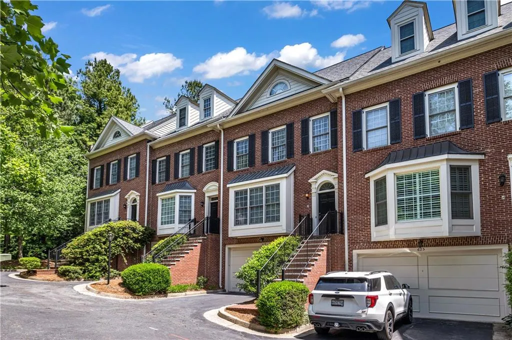 Brick townhome exterior featuring multiple bay windows, black shutters, dormer windows, and attached garages