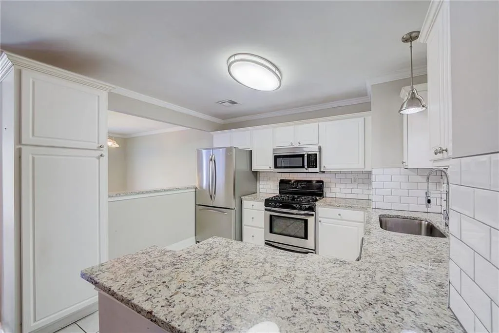 Kitchen with decorative light fixtures, appliances with stainless steel finishes, white cabinets, backsplash, and sink