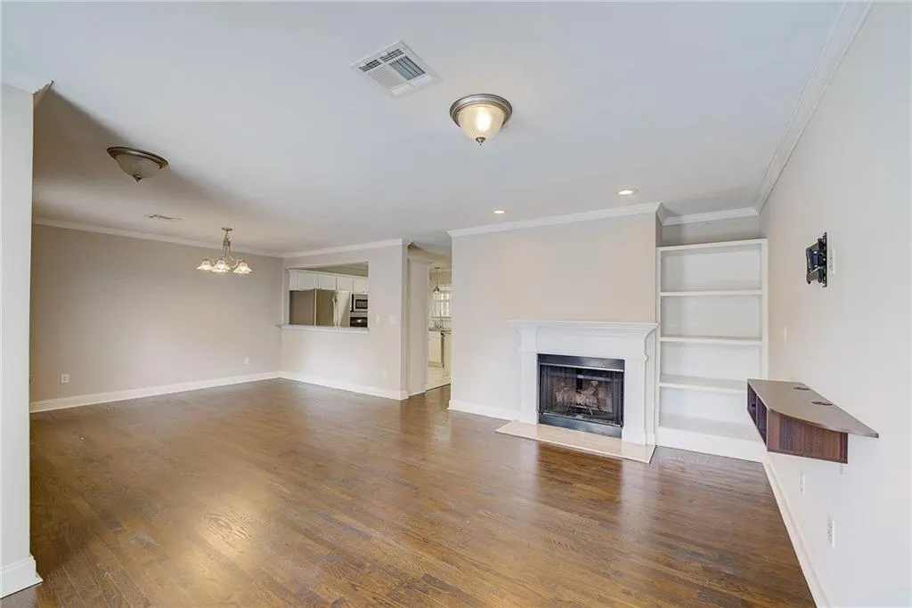 Unfurnished living room with a chandelier, crown molding, built in features, and dark hardwood / wood-style flooring