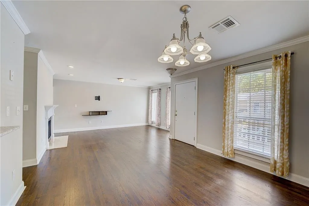Unfurnished living room featuring a notable chandelier, crown molding, and dark wood-type flooring
