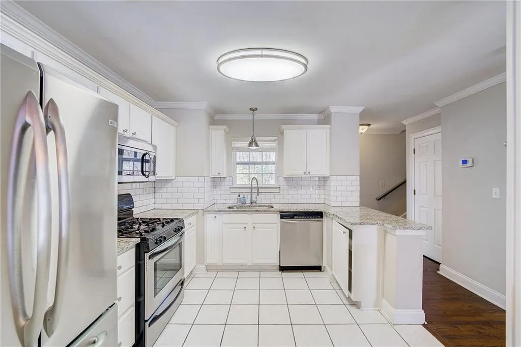 Kitchen with kitchen peninsula, appliances with stainless steel finishes, white cabinetry, light stone counters, and sink