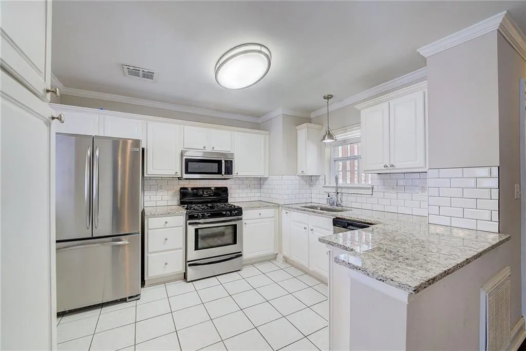 Kitchen with sink, light tile floors, white cabinets, stainless steel appliances, and tasteful backsplash