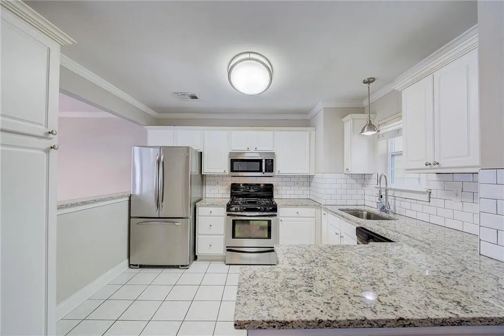 Kitchen featuring appliances with stainless steel finishes, backsplash, decorative light fixtures, sink, and white cabinets