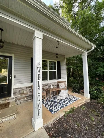 Covered porch featuring a natural stone facade, light-colored siding, and white columns