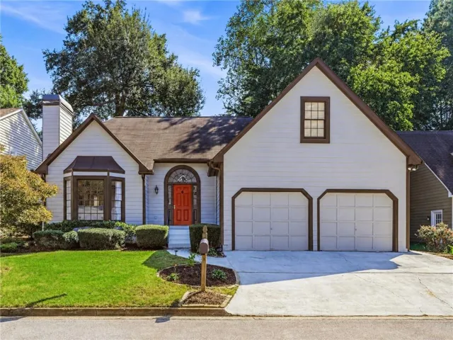 White siding exterior with a brown shingle roof, featuring a bright orange entry door with an arched transom window