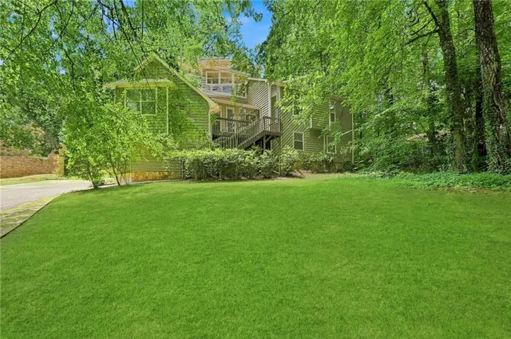 Expansive green lawn with mature trees and a multi-level wood-sided residence featuring an exterior staircase and multiple windows