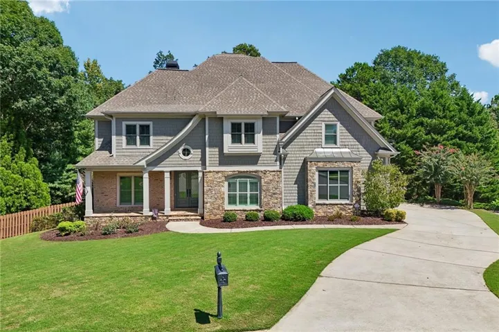 Stone and shingle exterior with brick accents, covered front porch, concrete driveway, and manicured landscaping