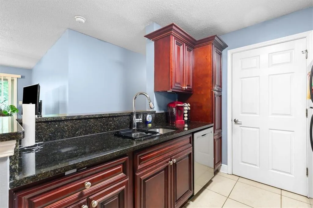 Kitchen featuring sink, dark stone countertops, light tile floors, and white dishwasher