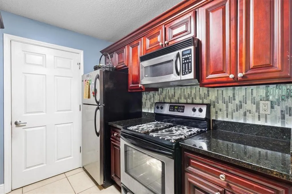 Kitchen with appliances with stainless steel finishes, light tile flooring, and dark stone countertops