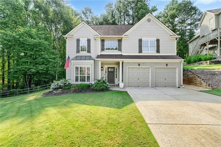 Two-story residence with light gray siding and dark shutters, featuring a two-car garage