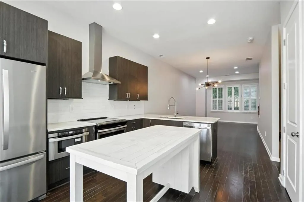 Kitchen with stainless steel appliances, wall chimney range hood, a peninsula, light countertops, and recessed lighting