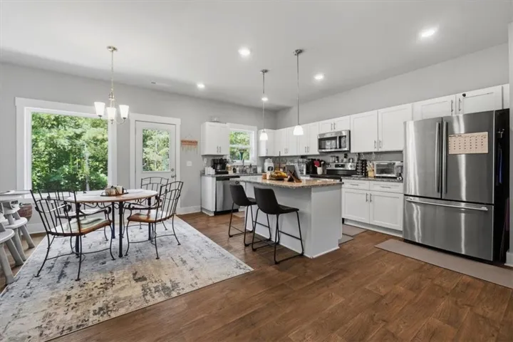 Open-concept kitchen and dining area featuring wood-finish flooring, white cabinetry, stainless steel appliances, and a kitchen island with seating