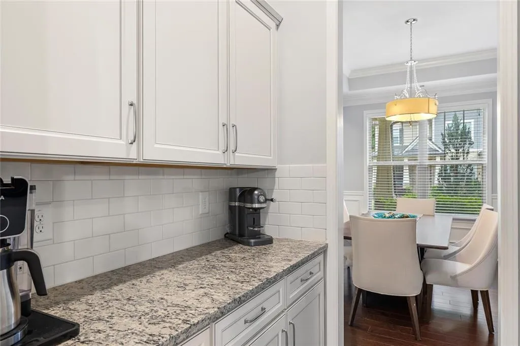 Kitchen with white cabinets, white backsplash, light stone countertops, and hardwood flooring
