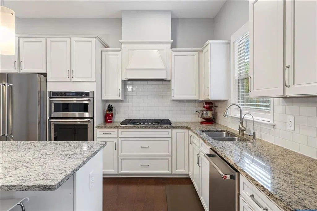 Kitchen featuring hardwood floors, white backsplash, custom exhaust hood, appliances with stainless steel finishes, and sink