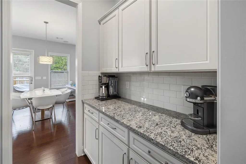 Kitchen featuring decorative light fixtures, light stone countertops, white backsplash, and hardwood floors