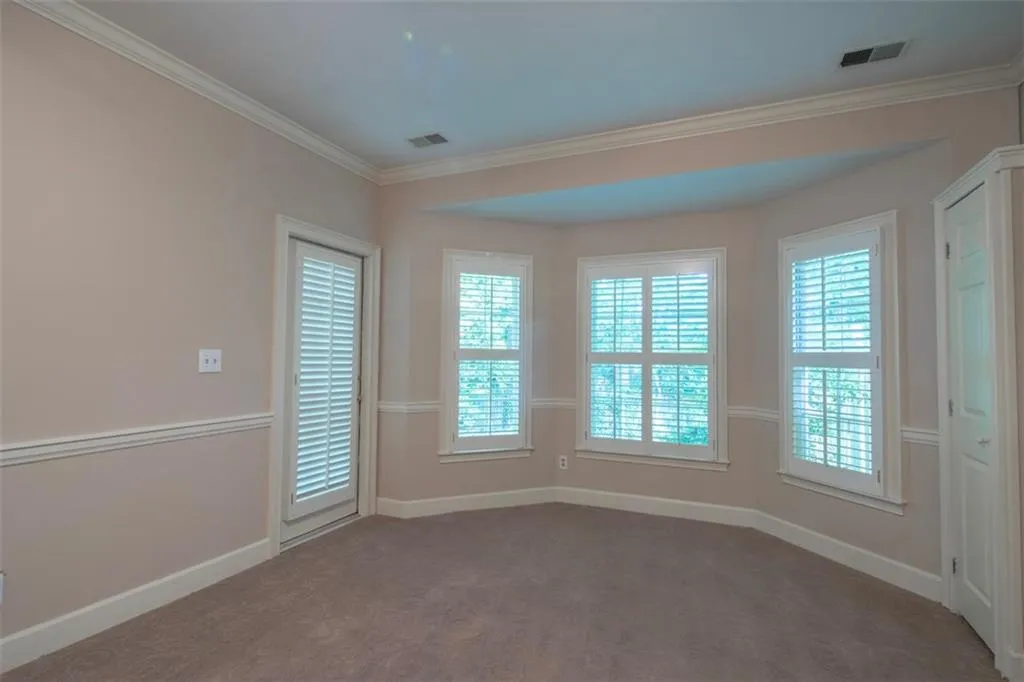 Empty room with ornamental molding, a healthy amount of sunlight, and carpet