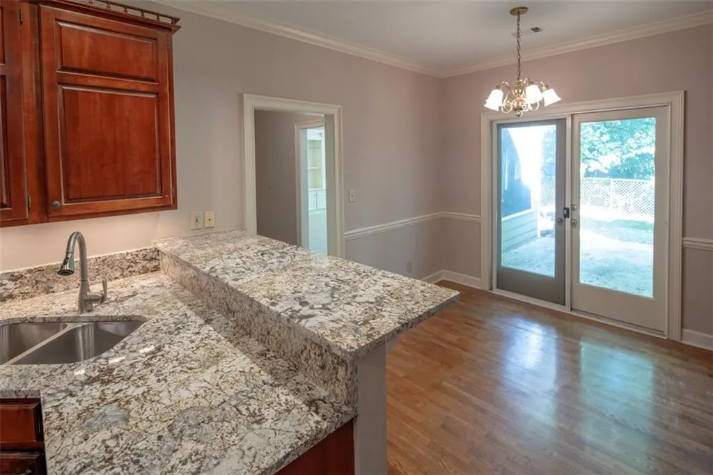 Kitchen with crown molding, hardwood / wood-style floors, a chandelier, sink, and light stone counters
