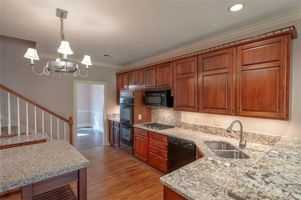 Kitchen with decorative light fixtures, light hardwood / wood-style flooring, black appliances, sink, and a notable chandelier