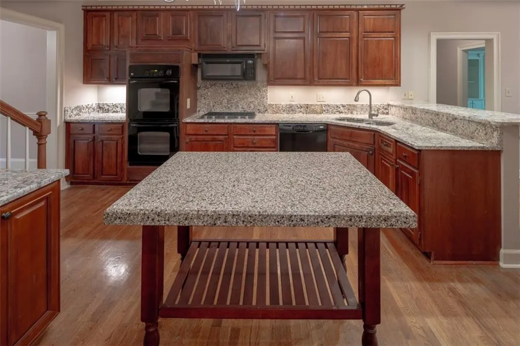 Kitchen featuring light stone countertops, light hardwood / wood-style flooring, black appliances, tasteful backsplash, and sink