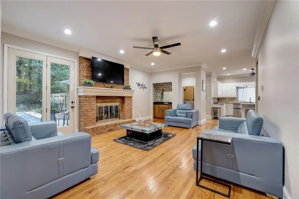 Living room with a brick fireplace, brick wall, light hardwood / wood-style flooring, ornamental molding, and ceiling fan